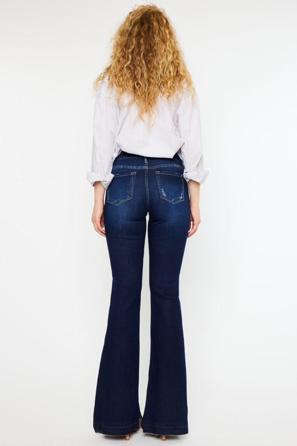 Woman wearing Kancan mid rise slim flare dark stonewash jeans with white shirt and sandals.