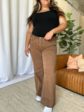 Woman wearing brown RFM Full Size High Rise Garment Dye Wide Leg Jeans with raw hem and black top indoors